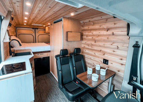 Explore this modern RV rental interior featuring a bed, kitchenette with sink & cooktop, and dining area. Comfort on the road!