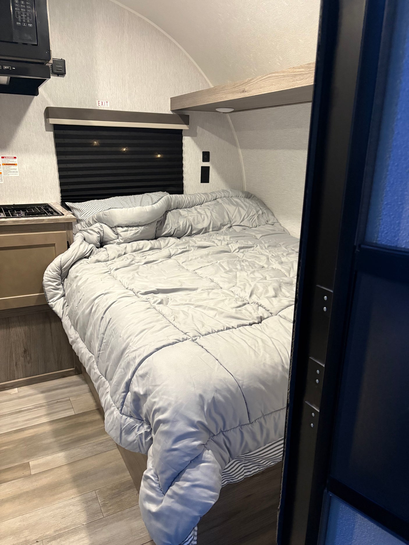 RV rental interior: A compact bedroom with a grey bedspread, small kitchen counter, stove, microwave, and wood flooring.