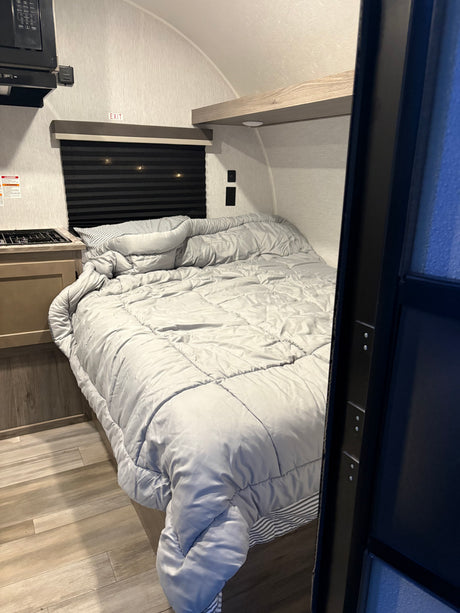 RV rental interior: A compact bedroom with a grey bedspread, small kitchen counter, stove, microwave, and wood flooring.