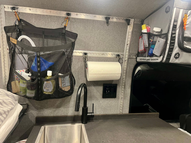 RV rental interior: sink, black faucet, mesh organizers, and charging station against gray walls for compact living. — photo 18