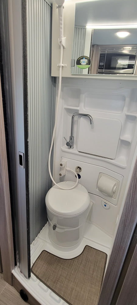 This compact RV rental wet bath features a white toilet, integrated sink with a chrome faucet, and a handheld shower head.