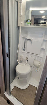 This compact RV rental wet bath features a white toilet, integrated sink with a chrome faucet, and a handheld shower head.