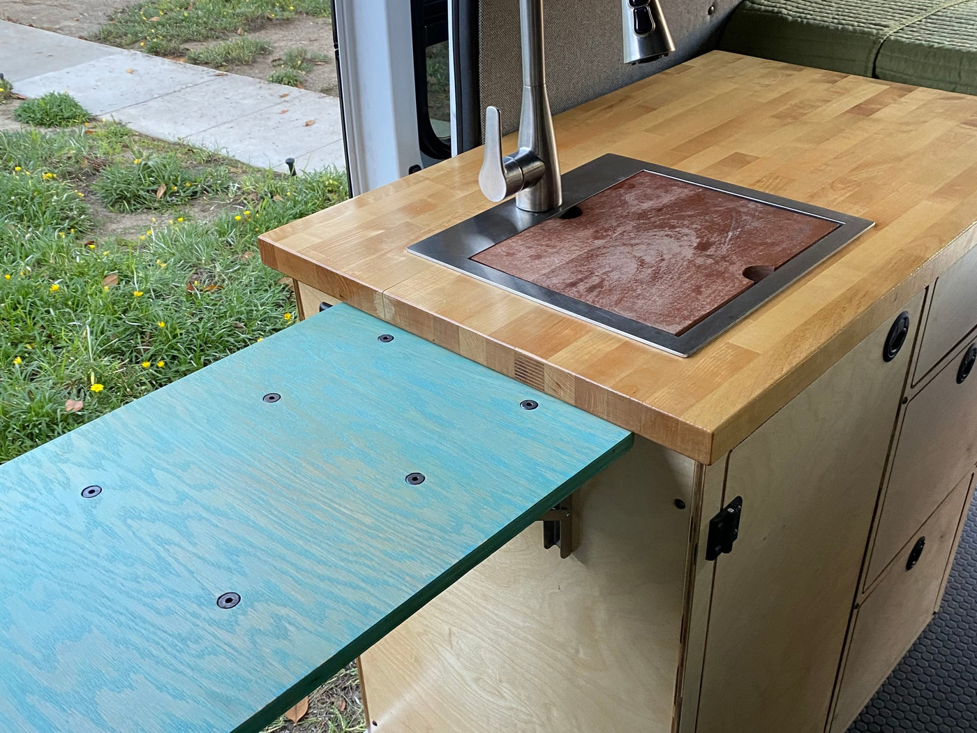 RV rental van's kitchen: wood countertop, sink with cutting board, faucet, and a turquoise pull-out table for smart space. — photo 17