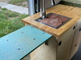 RV rental van's kitchen: wood countertop, sink with cutting board, faucet, and a turquoise pull-out table for smart space.