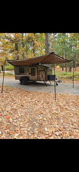 RV rental teardrop camper with awning, parked in a vibrant autumn forest campsite covered in fall leaves.