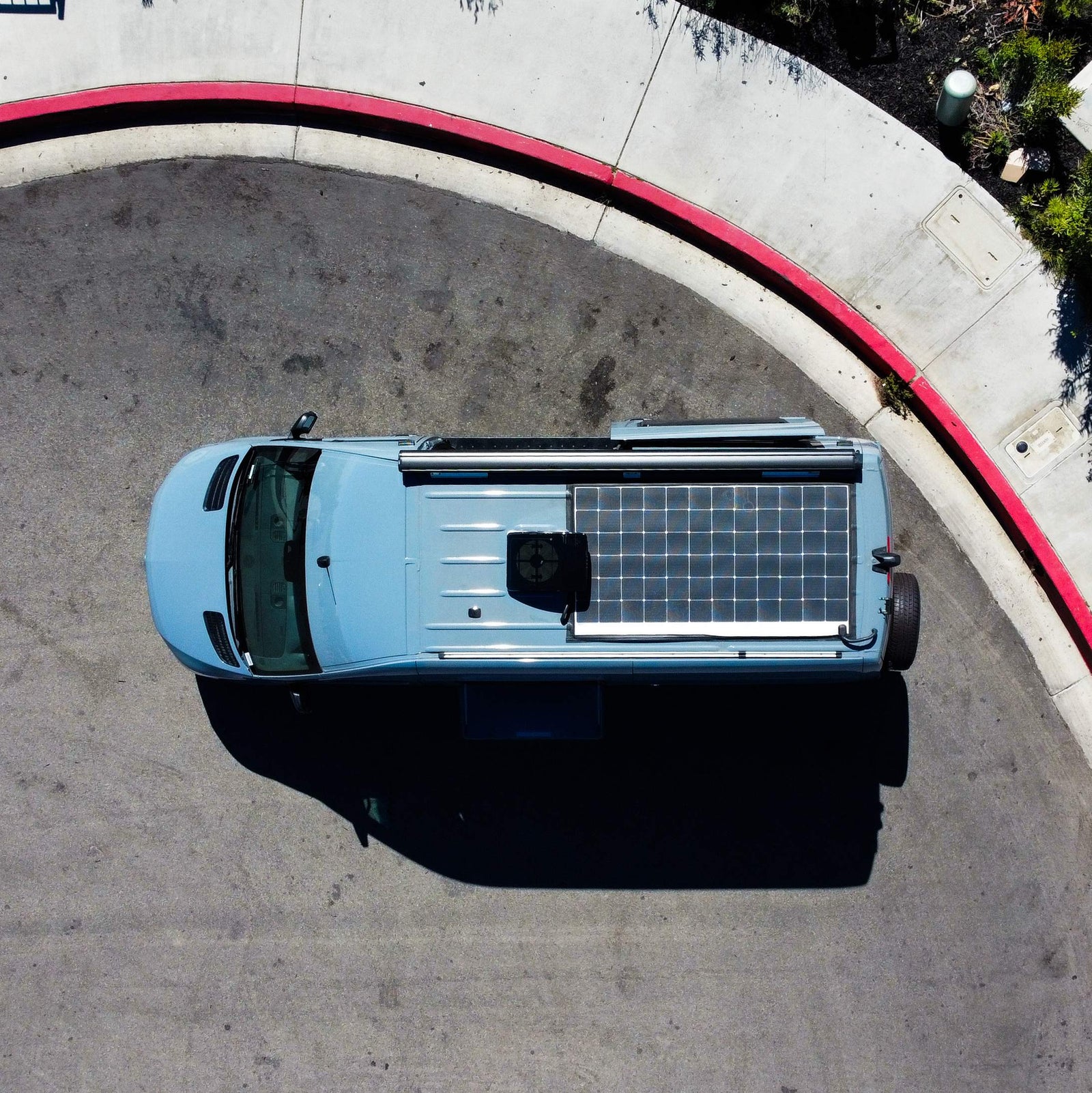 Aerial view: light blue camper van with solar panels, parked by a red curb. Ideal for your next RV rental.