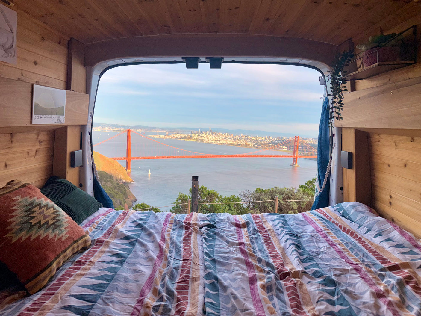 An rv rental's cozy bed offers panoramic views of the Golden Gate Bridge and San Francisco Bay from inside a wooden camper van.