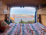 An rv rental's cozy bed offers panoramic views of the Golden Gate Bridge and San Francisco Bay from inside a wooden camper van.