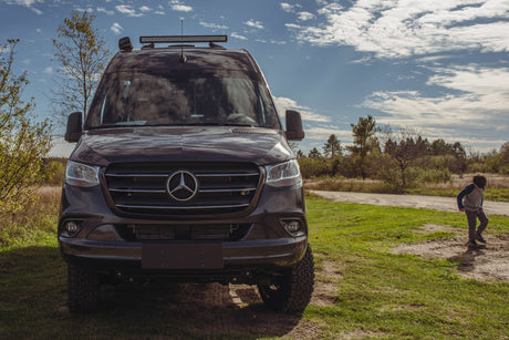 Our rugged Mercedes-Benz Sprinter RV rental, featuring off-road tires and a light bar, is ready for adventure. A boy walks nearby.