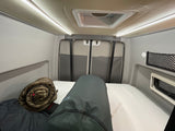 Cozy **RV rental** interior: a bright bedroom area with a white mattress, overhead lights, and rear doors.