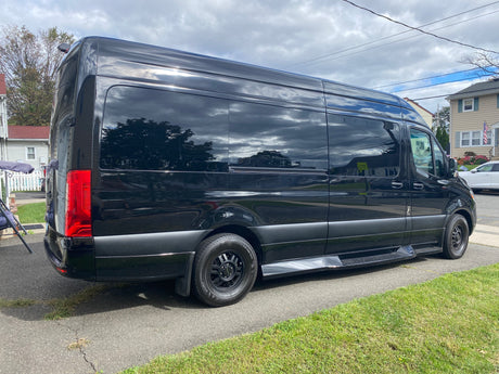 Sleek black RV rental van, a large Mercedes-Benz Sprinter, parked on asphalt, showcasing tinted windows.