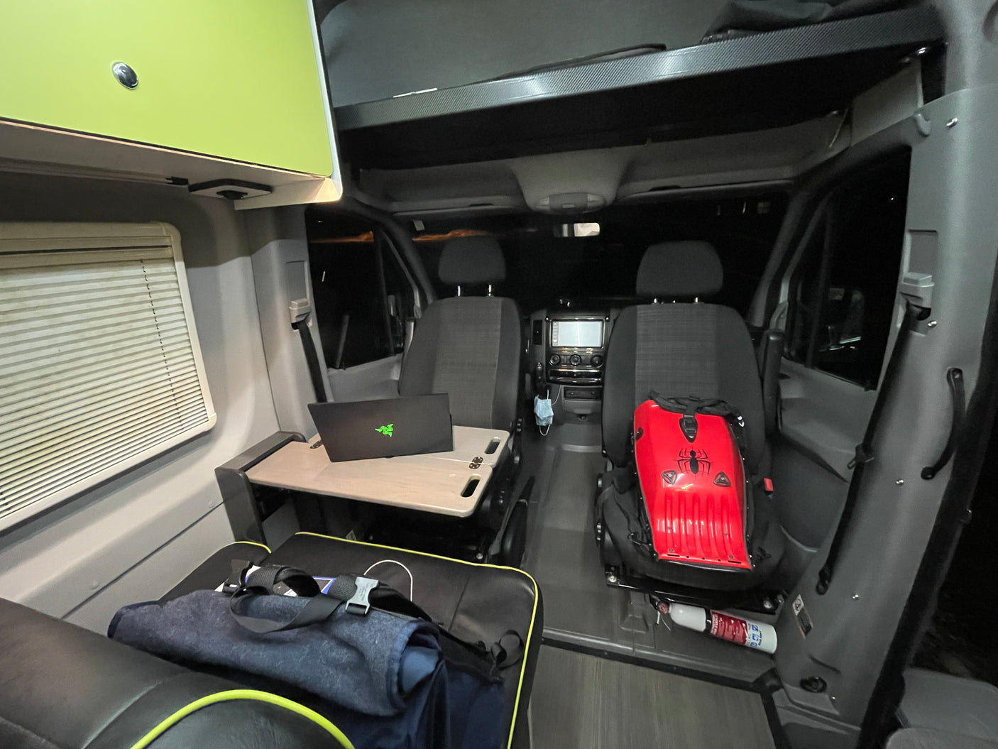 An RV rental interior, showing a mobile office setup with a laptop, passenger seats, and overhead storage.
