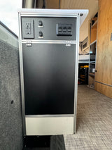 RV rental interior control panel with AC/USB outlets and switches for pump/flush systems, providing onboard utilities.
