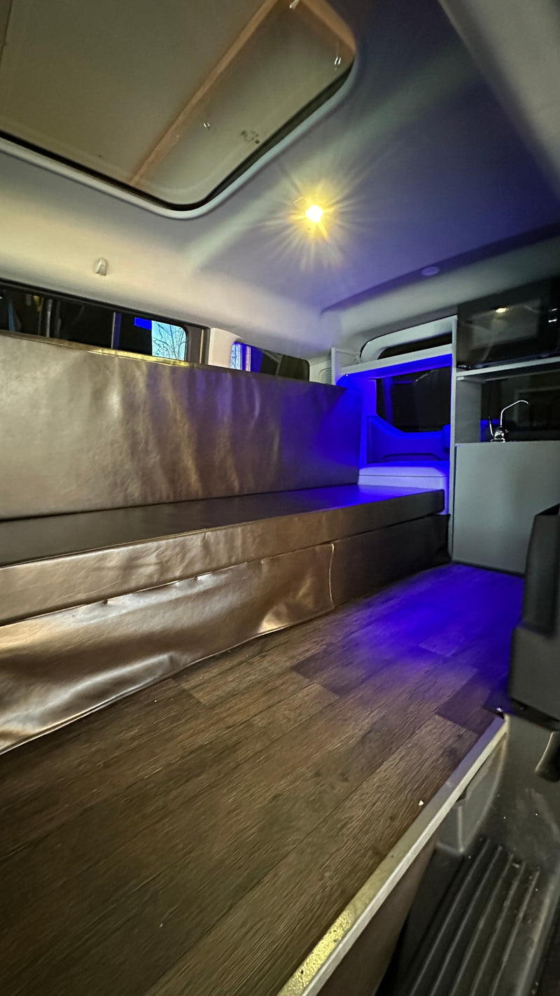 Inside a modern RV rental: dark wood flooring, comfortable seating/bed, kitchenette, and blue ambient lighting. — photo 4