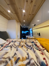 Cozy RV rental interior with a comfortable bed, warm wood ceiling, and compact kitchen.