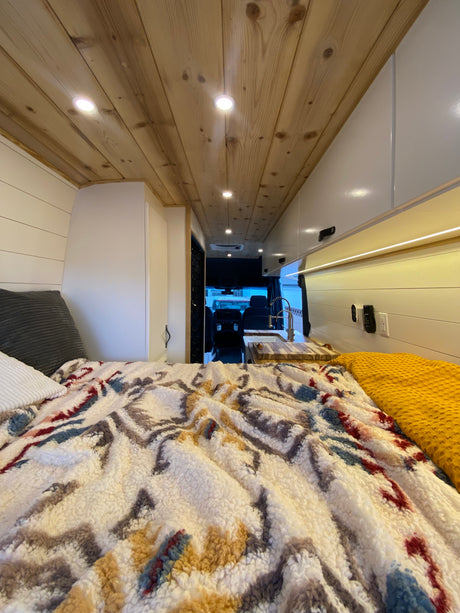 Cozy RV rental interior with a comfortable bed, warm wood ceiling, and compact kitchen.