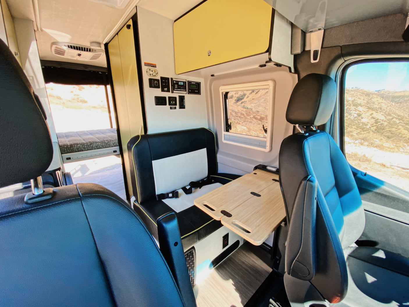 Step inside this cozy RV rental! Features a dinette with portable table, main seating, and control panel. A bed is visible in the rear.