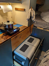 RV rental kitchen: Induction cooktop, pot, and pull-out cooler in a compact camper interior with a bed visible.