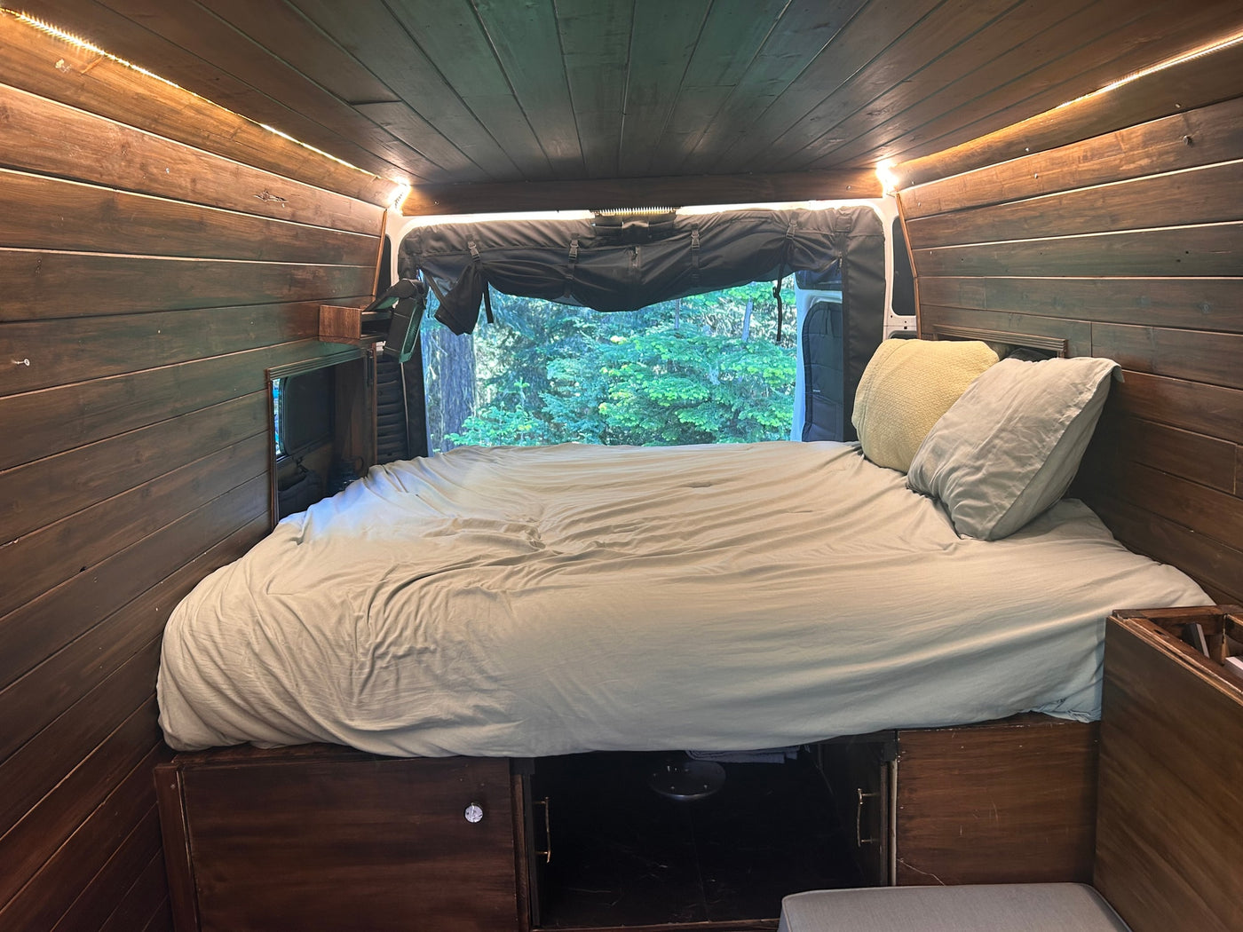 This cozy RV rental features a comfortable bed, wooden interior paneling, warm LED lighting, and a beautiful forest view. — photo 12