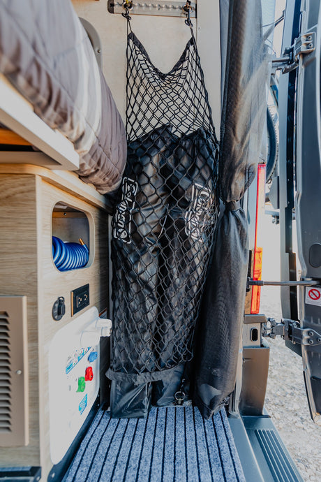 RV rental interior featuring a bed, clever cargo net storage, and utility panel with hose in a camper van.