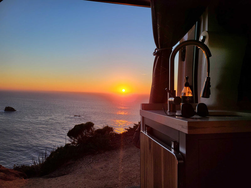 Vibrant sunset over the ocean from an RV rental camper van. Inside, a kitchen sink, faucet, and soap bottle are visible. — photo 15