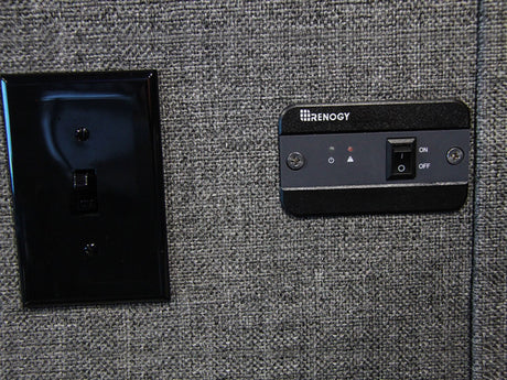 RV rental power control: A black light switch & Renogy panel with ON/OFF switch & indicator lights on a grey wall.