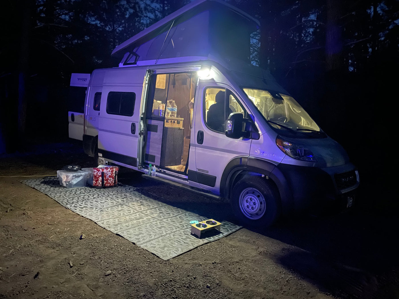 Nighttime RV rental setup: a bright camper with pop-top extended, open door showing interior, and outdoor mat for comfortable camping. — photo 5