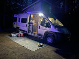 Nighttime RV rental setup: a bright camper with pop-top extended, open door showing interior, and outdoor mat for comfortable camping.