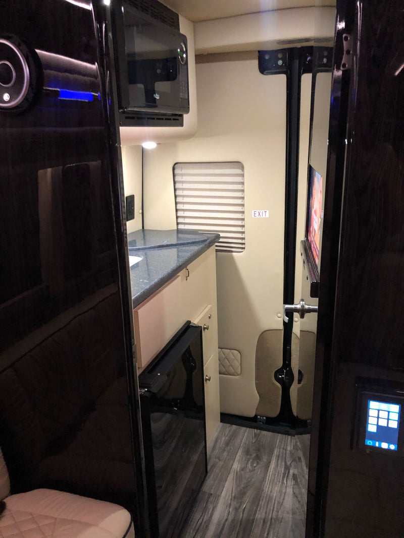 Compact RV rental interior featuring a functional kitchenette with microwave, TV, and integrated control panel. — photo 15