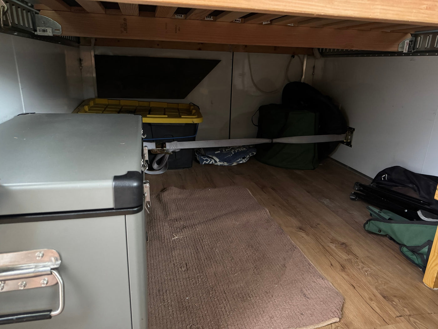 RV rental under-bed storage features a secured portable fridge, bins, and camping gear with a tie-down strap. — photo 8