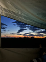 Relaxing inside an RV rental, admiring a stunning sunset through the window screen, showcasing a vibrant sky & distant horizon.