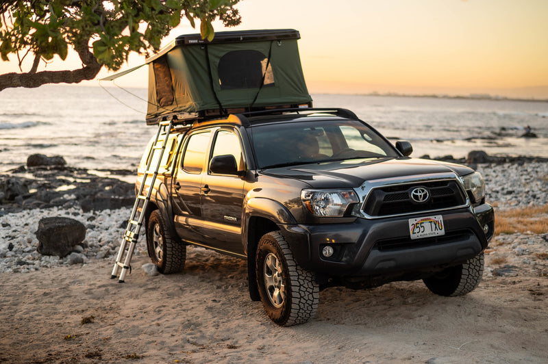  more versatile than a typical RV rental.|Adventure-ready RV rental truck perched on a rugged cliff overlooking the blue ocean. Ideal for exploring scenic coastal landscapes.|Coastal RV rental truck with rooftop tent and camp setup — photo 3