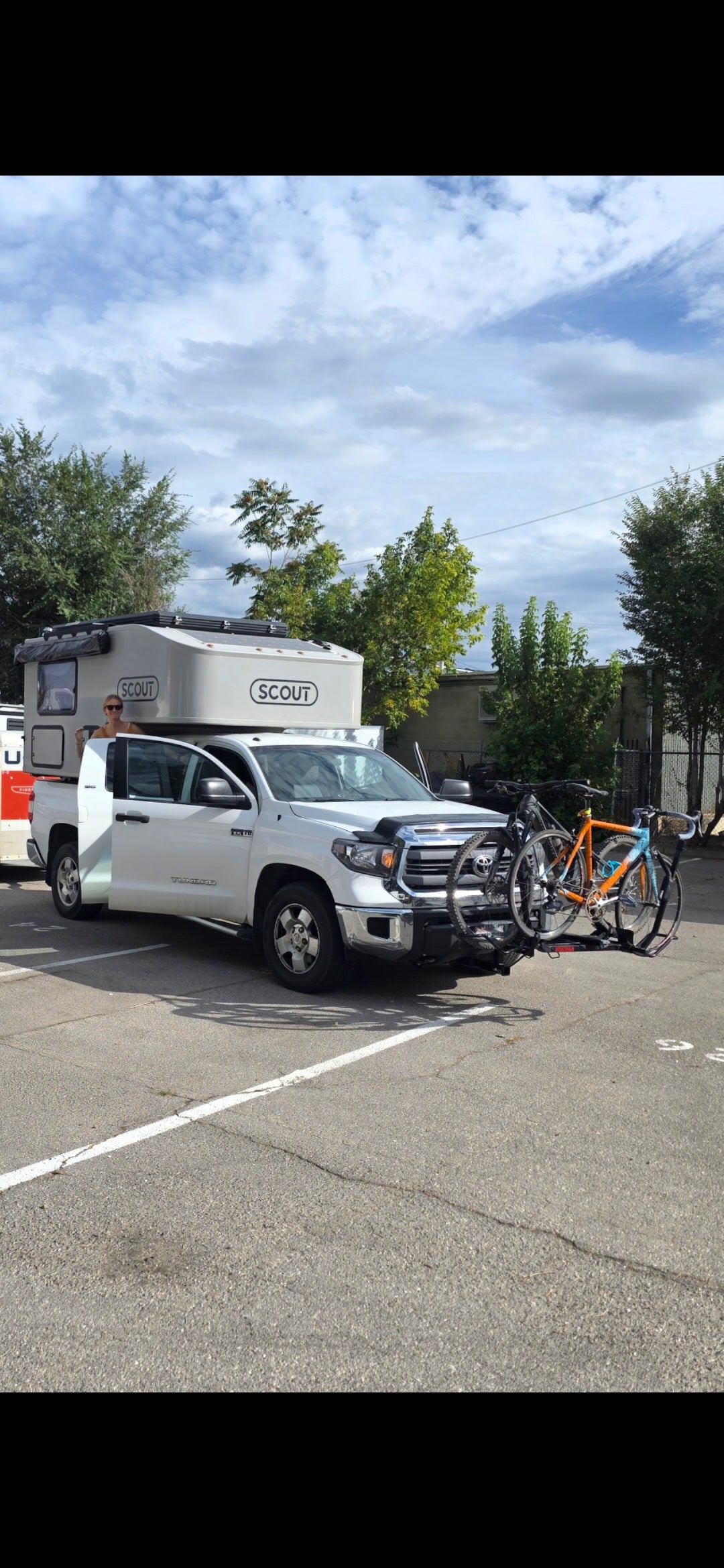 RV rental truck with a Scout camper, person in doorway, and two bikes on the front rack. Perfect for outdoor adventures!