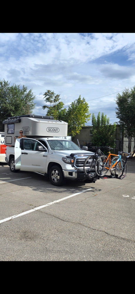 RV rental truck with a Scout camper, person in doorway, and two bikes on the front rack. Perfect for outdoor adventures!