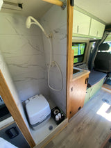 Compact RV rental interior: shower, portable toilet, and kitchenette space for mobile living.