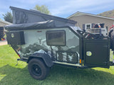 This rugged Mission Overland trailer, featuring mountain graphics, pop-up tent, and off-road tires, is ideal for your next RV rental adventure or off-road camping trip.