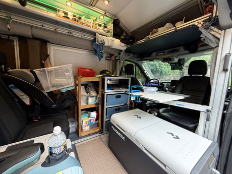Cozy RV rental interior with car seat, Dometic cooler, organized storage, and a convertible table for mobile living.