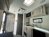 Spacious RV rental interior: modern kitchen with sink, stove, microwave, fridge, ceiling AC, and skylight.