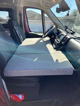 Compact RV rental camper van interior featuring a cleverly folded bed set up between the swivel front seats and dashboard, ready for sleeping.