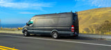 Dark gray Sprinter RV rental camper van, parked on a scenic mountain road overlooking a valley.