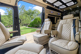 Luxurious RV rental interior with cream leather seats, featuring an open side door revealing a vibrant green yard, trees, and a house.