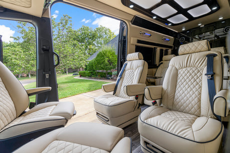 Luxurious RV rental interior with cream leather seats, featuring an open side door revealing a vibrant green yard, trees, and a house.