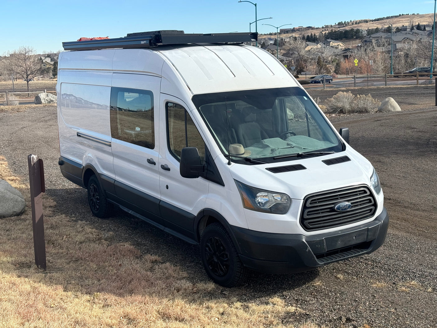 White Ford Transit van, converted for RV rental. Parked on gravel, ready for travel and outdoor adventures.