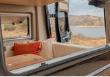 Serene rv rental camper interior with open doors to a scenic lake and mountain view. Cushions and table ready for adventure.