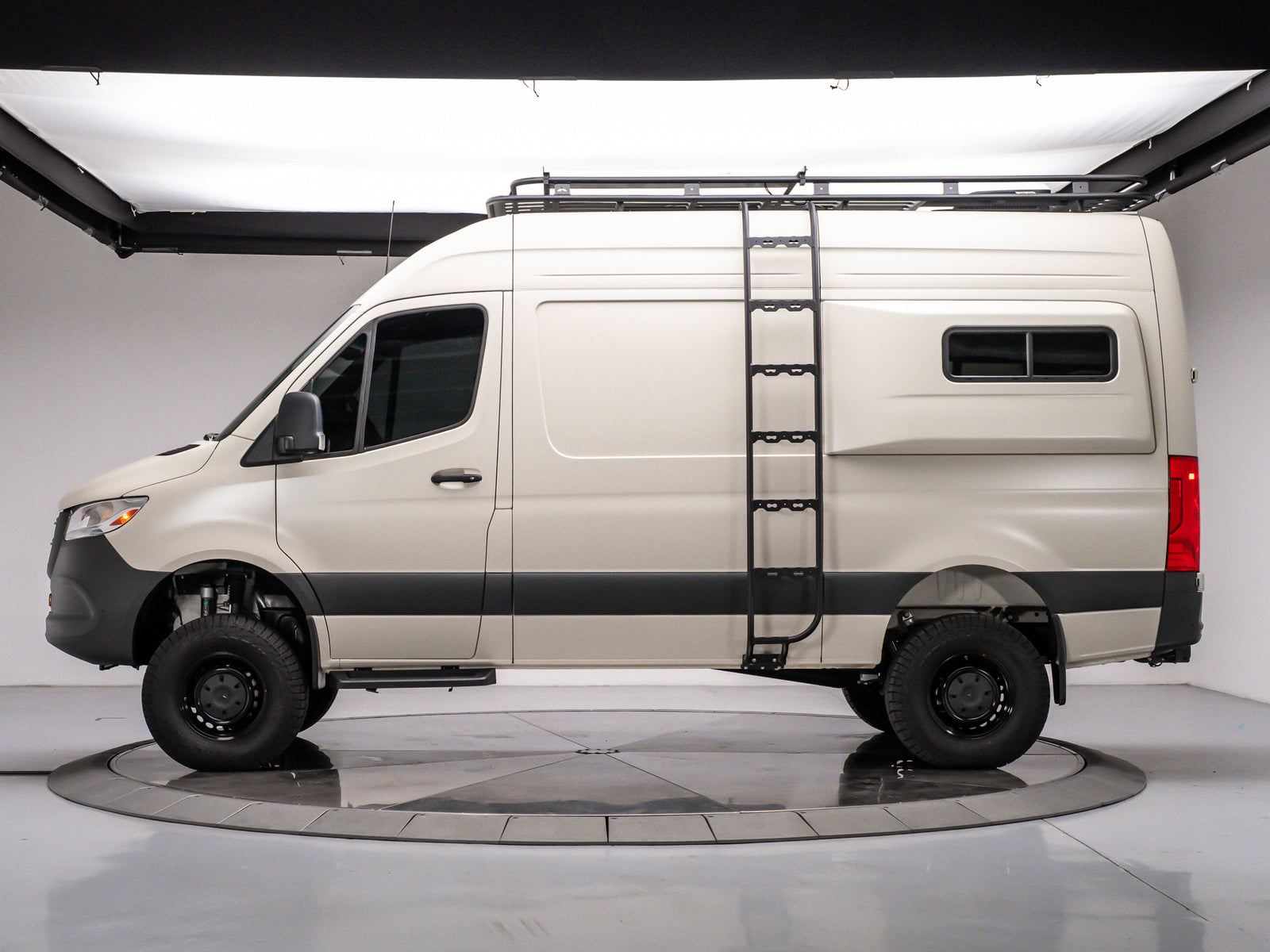 Side view of a tan Mercedes Sprinter rv rental camper van with a roof rack and ladder, on a studio turntable.