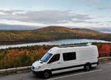 White rv rental camper van with solar panels, overlooking a stunning autumn lake and vibrant fall foliage.