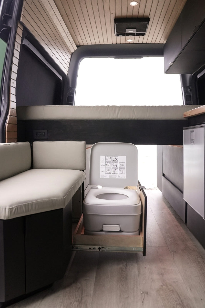 This RV rental features a cleverly designed interior with a pull-out portable toilet, bed, and cozy seating area. — photo 11