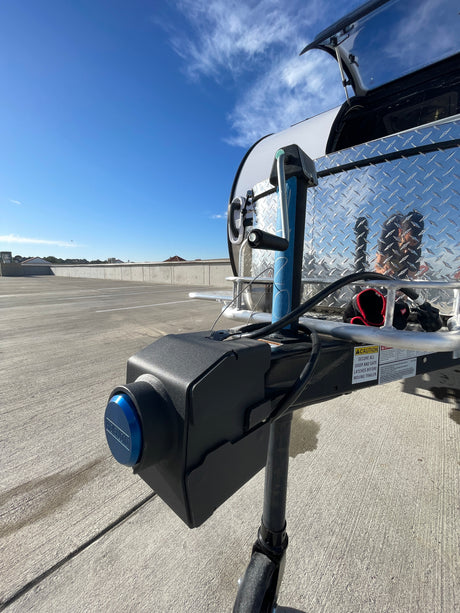 Front view of an RV rental trailer's hitch with a blue locking mechanism and warning label, parked on a concrete lot under a blue sky.