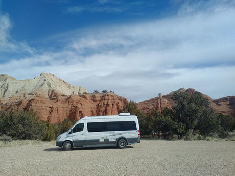 RV rental parked on gravel, showcasing stunning red and white desert mountains under a blue sky.