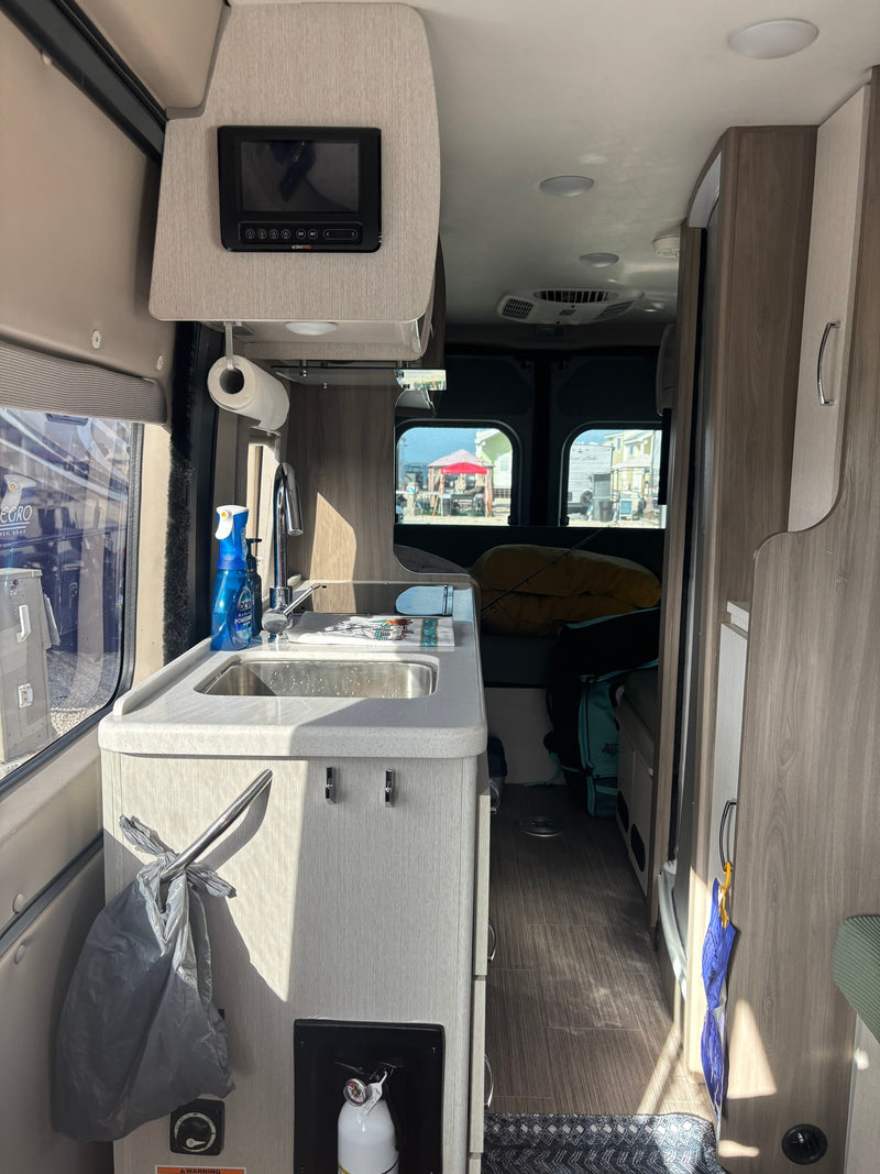 Interior of an rv rental, featuring a compact kitchen with a sink, overhead control panel, and an outdoor campsite view. — photo 6
